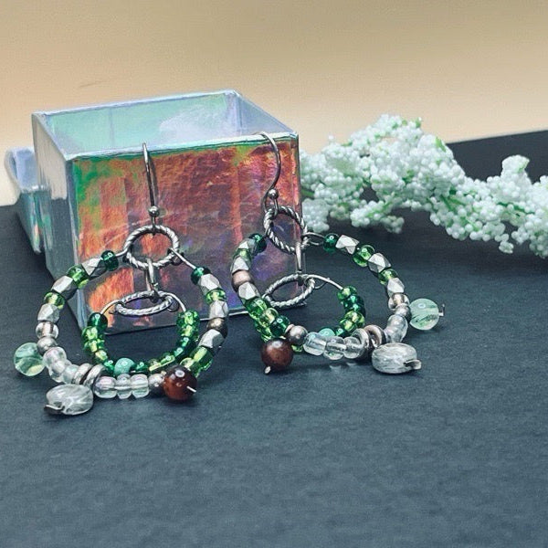 Beaded earrings on a dark surface with a decorative box and greenery in the background