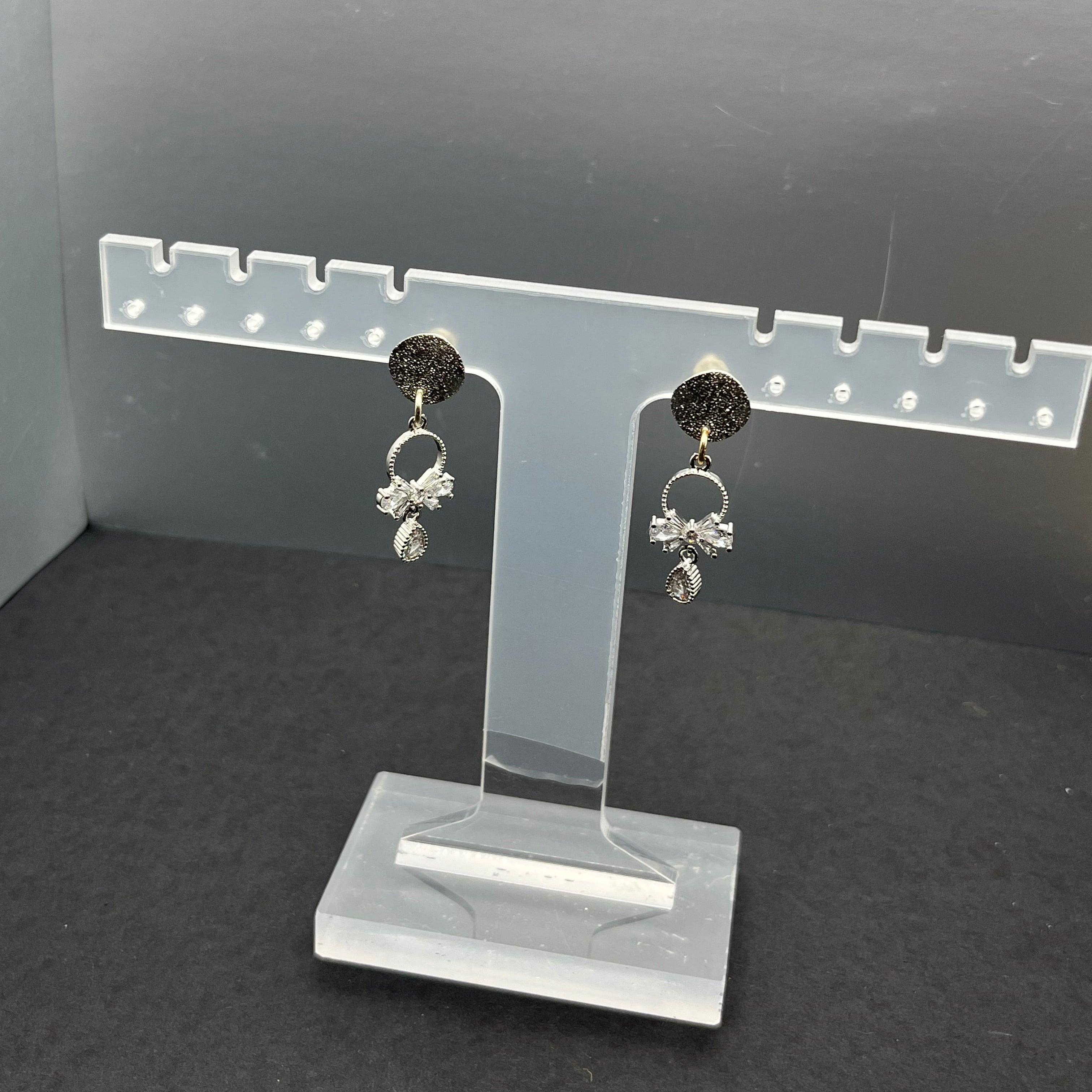 Pair of sterling silver bow dangle earrings on a clear stand against a dark background
