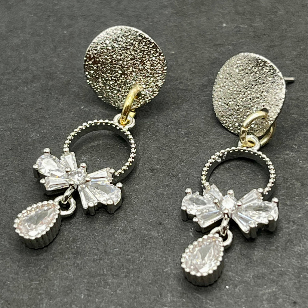 Pair of silver earrings with bow and teardrop designs on a dark background
