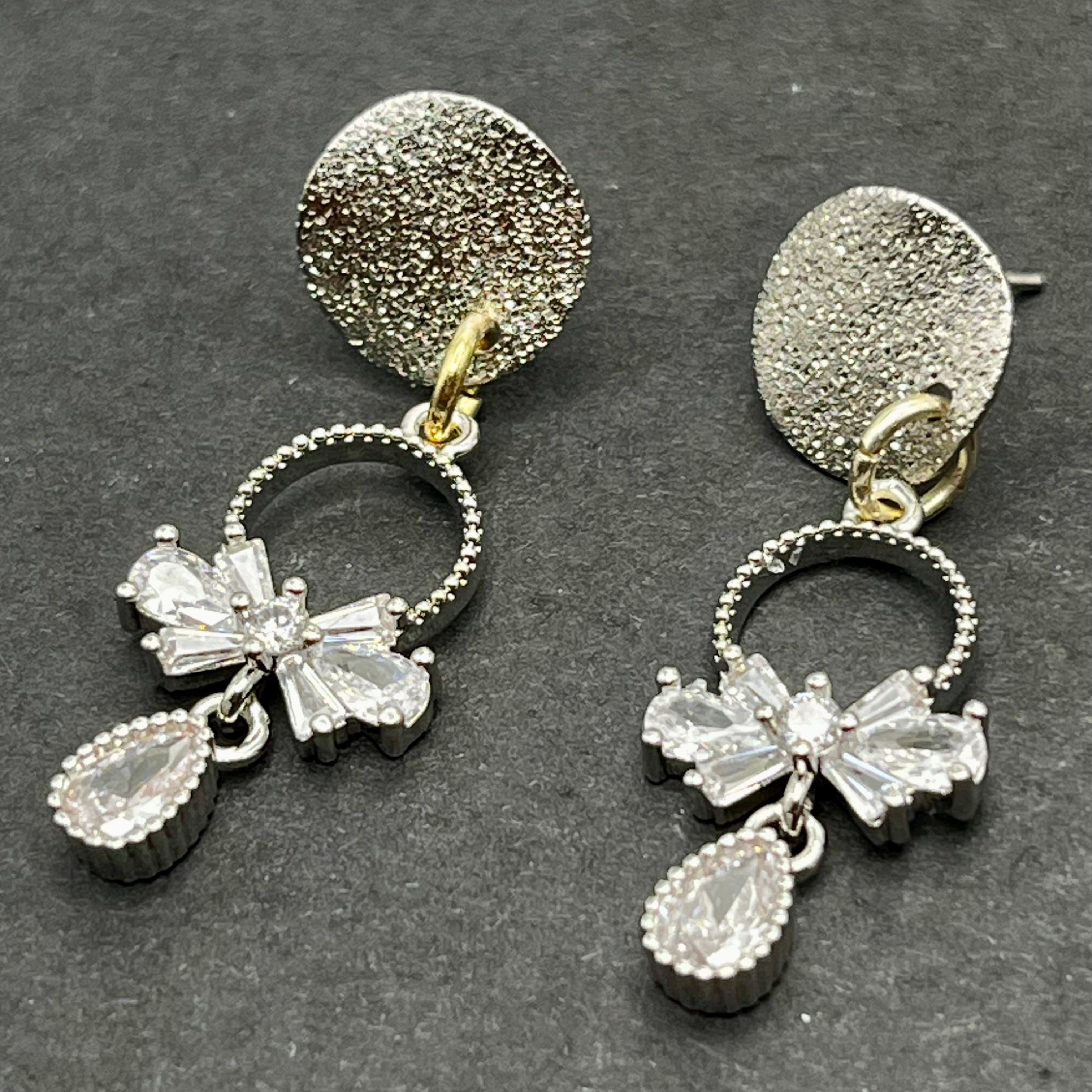 Pair of silver earrings with bow and teardrop designs on a dark background